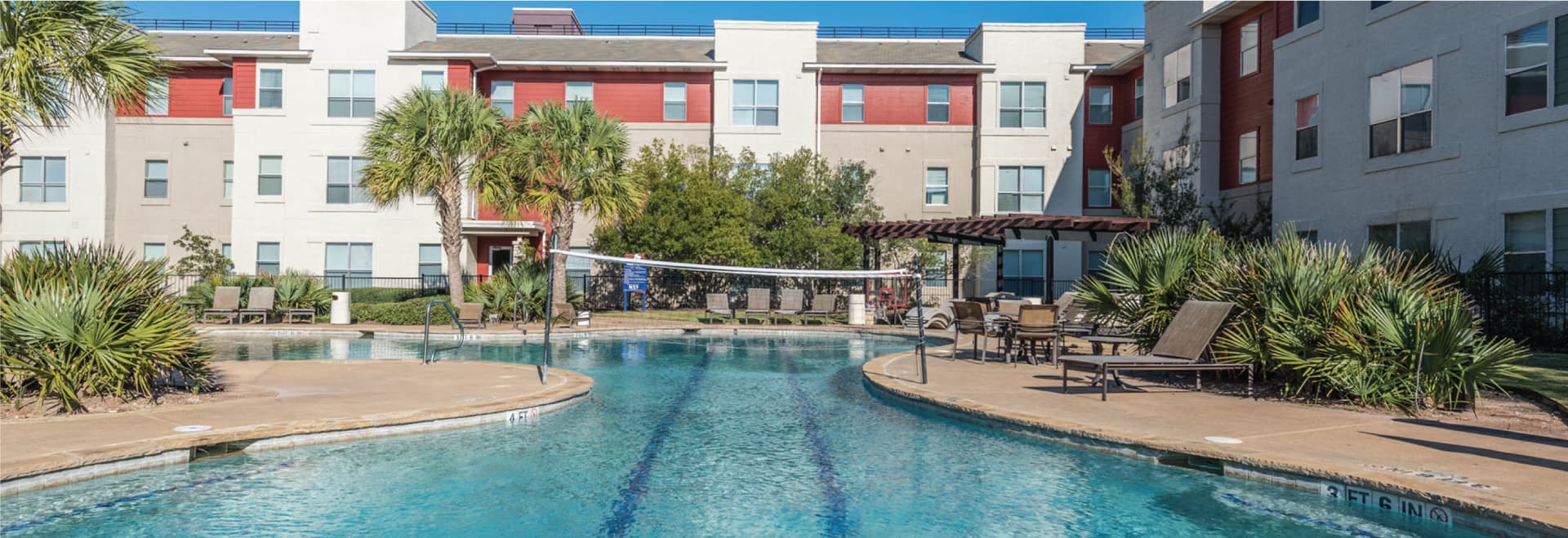 Apartment courtyard with a large hourglass shaped swimming pool with pergola, lounge seating, palm trees