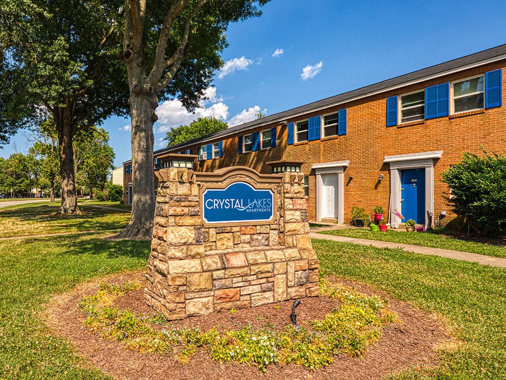 Apartment community with a brick exterior and a stone sign that reads 'Crystal Lakes Apartments.'